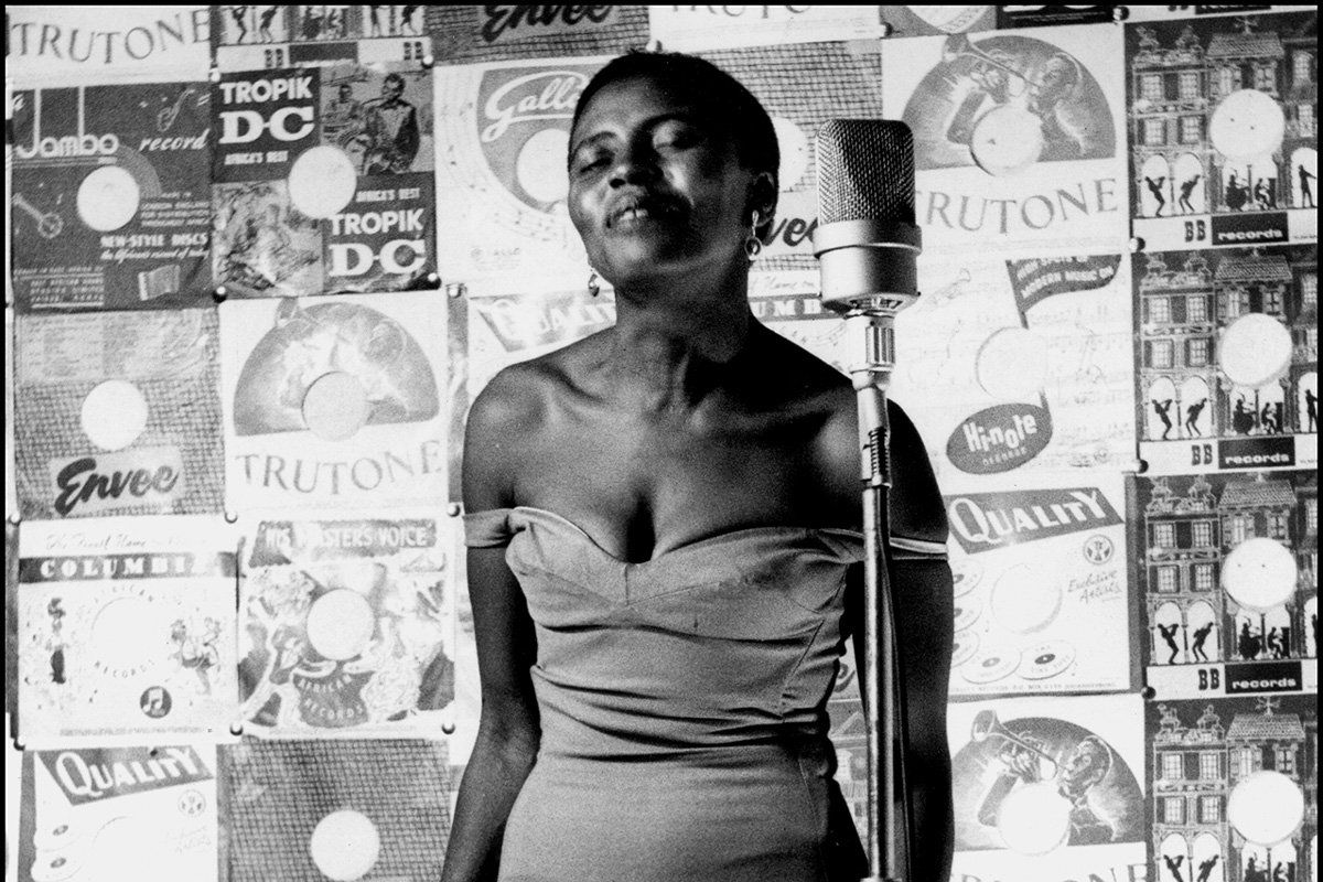 A black and white image of Miriam Makeba standing with her eyes closed in front of a microphone.