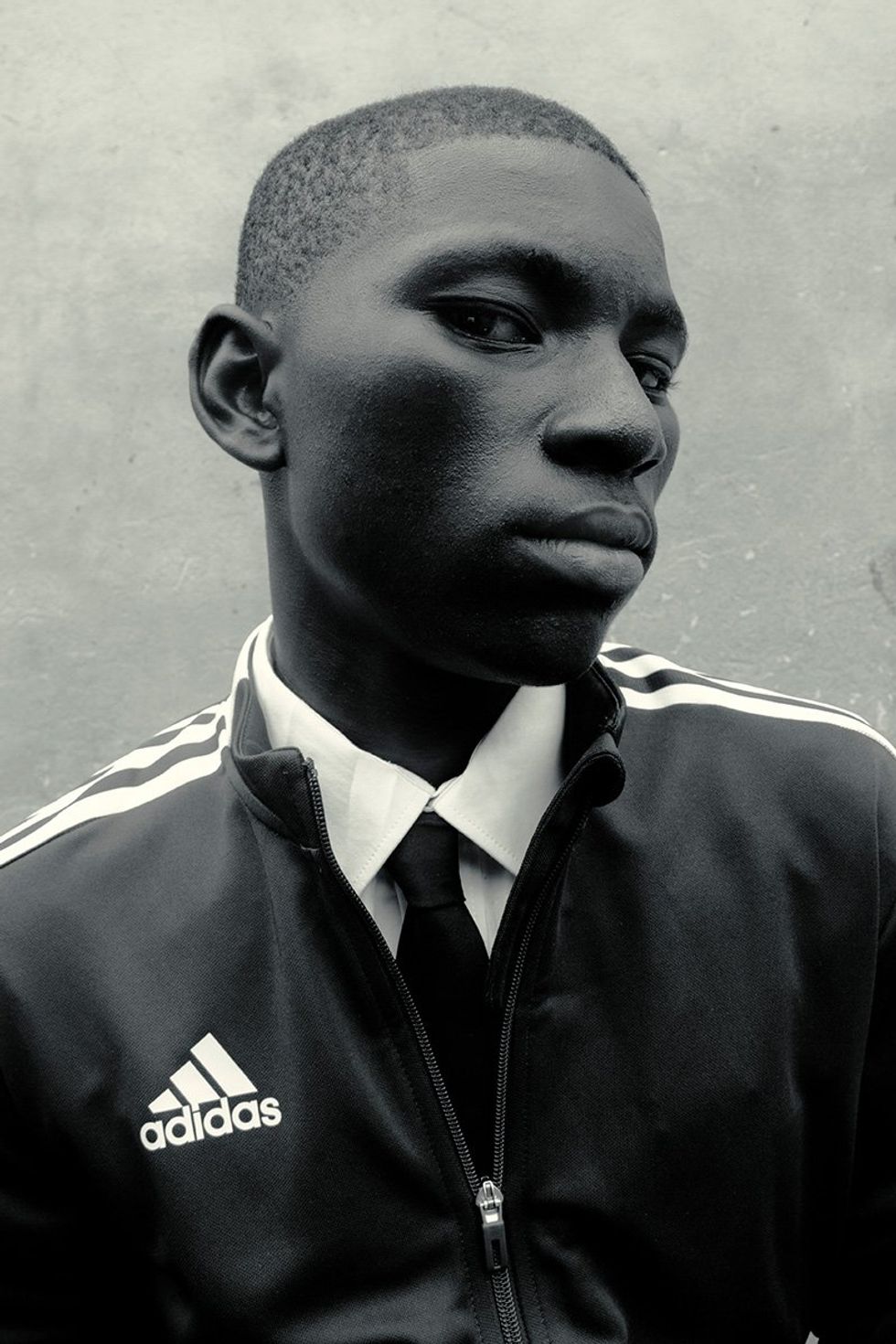 A black and white image taken by the photographer of a young boy wearing an Adidas jacket over a tie. 