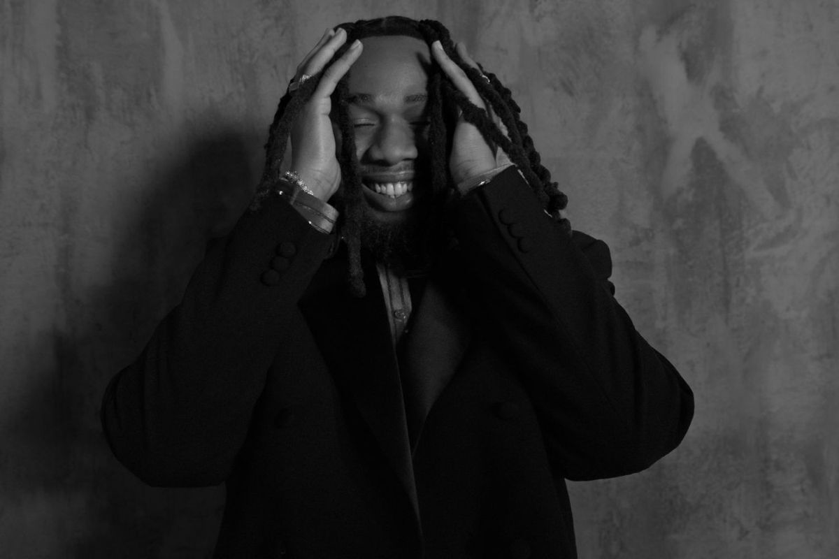 A black and white picture of Bnxn wearing a suit, with his hands tousling his hair.