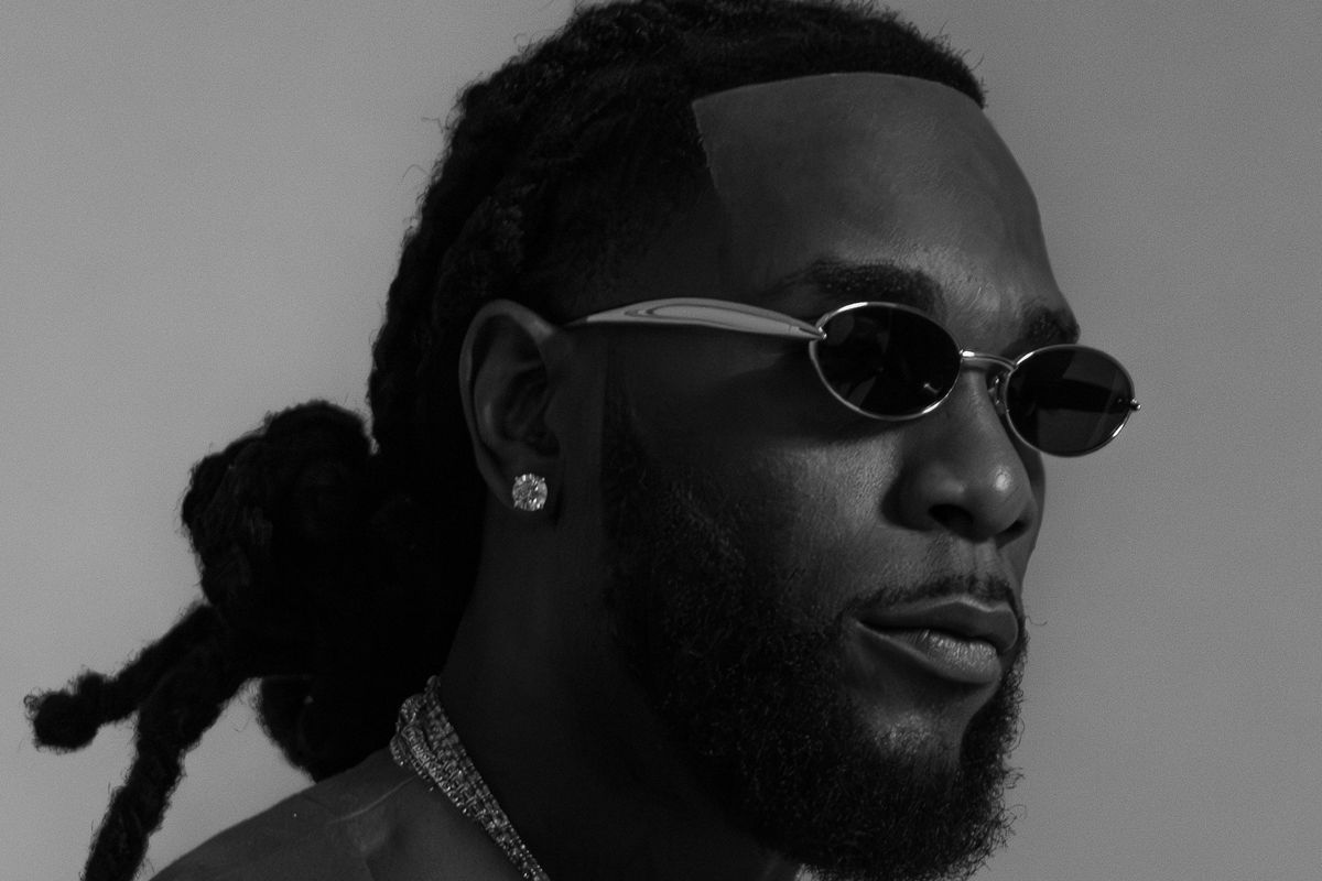 A black and white portrait photo of Burna Boy wearing stylish glasses and silver jewelry.