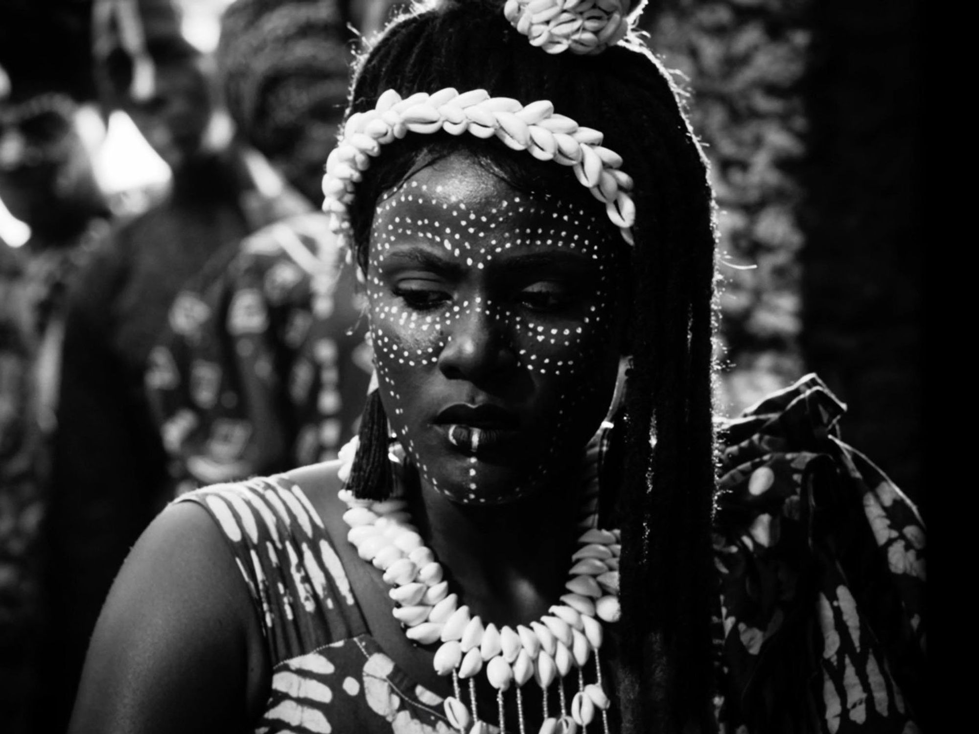 A black and white still from the film, Mami Wata, directed by CJ Obasi of a woman with Yoruba face paint on, looking with her eyes downcast.
