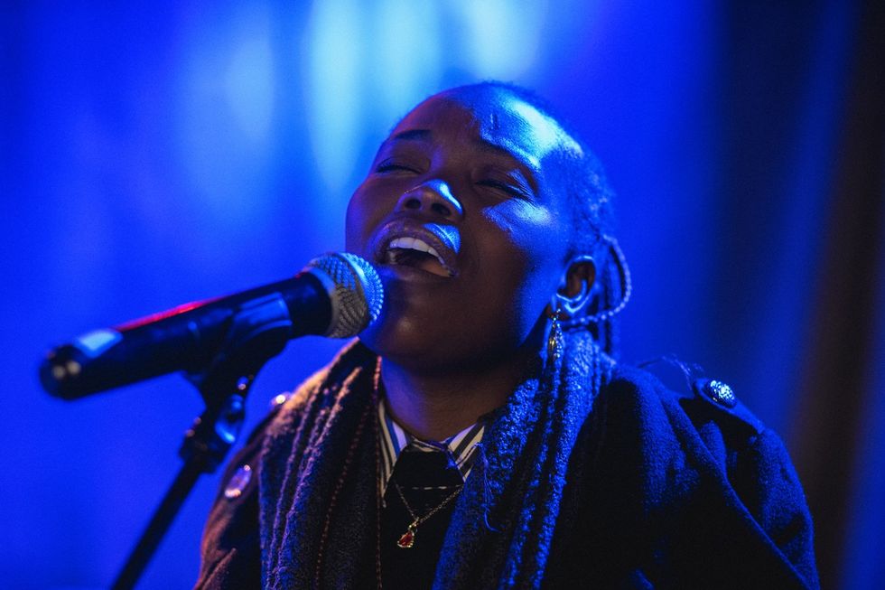 A Black woman sings with her eyes closed under blue lights. 