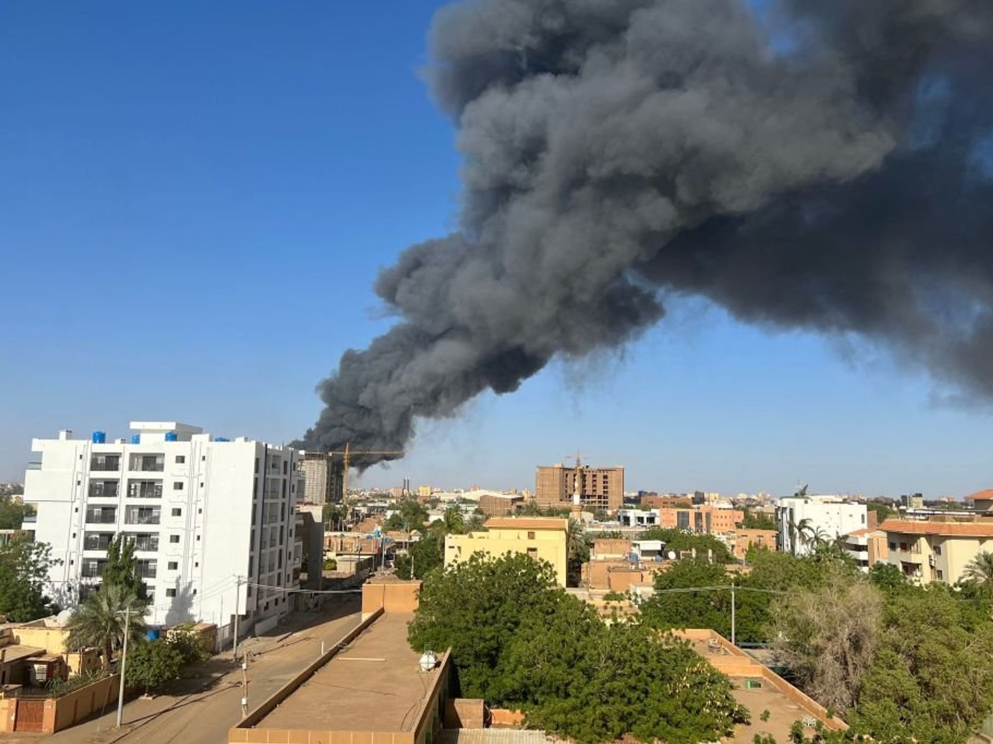 ​A column of smoke rises behind buildings near the airport area in Khartoum on April 19, 2023, amid fighting between the army and paramilitaries following the collapse of a 24-hour truce.