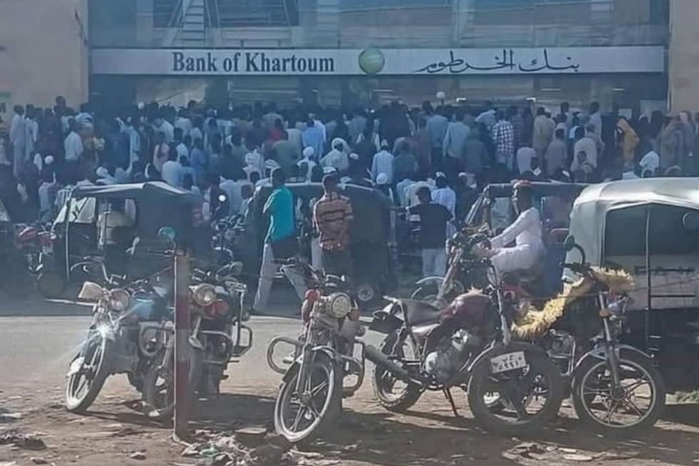 A crowd of people standing outside a bank in a dusty street in Port Sudan.
