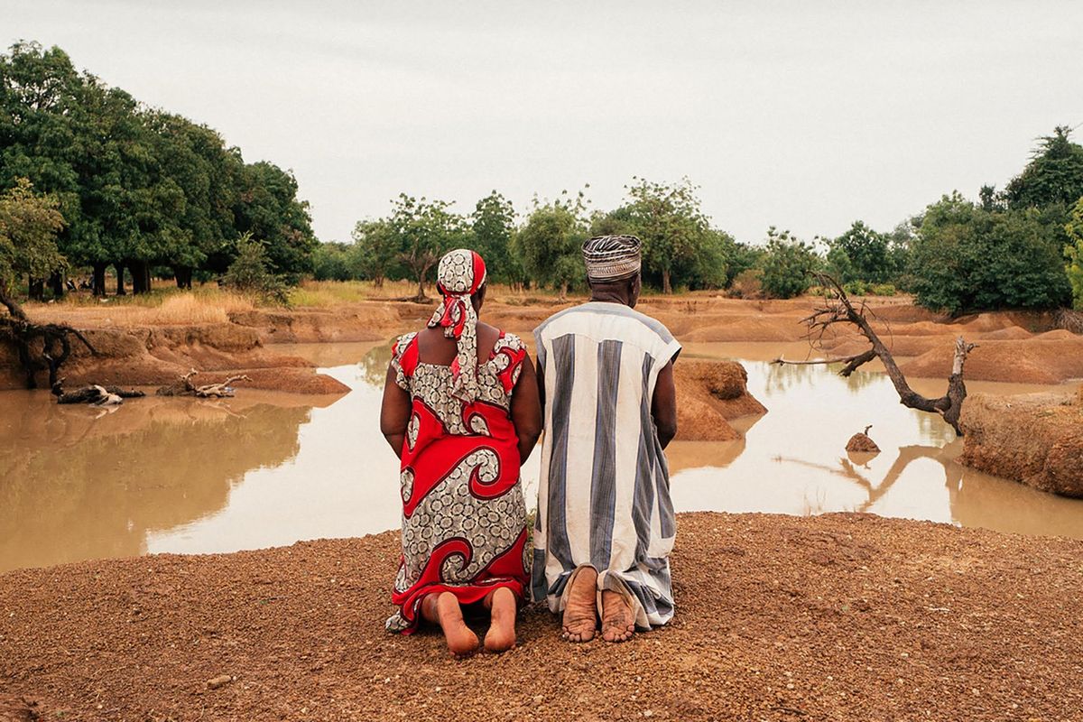 A film still from 'Bravo, Burkina!' of a man and a woman kneeling at a small lake. 