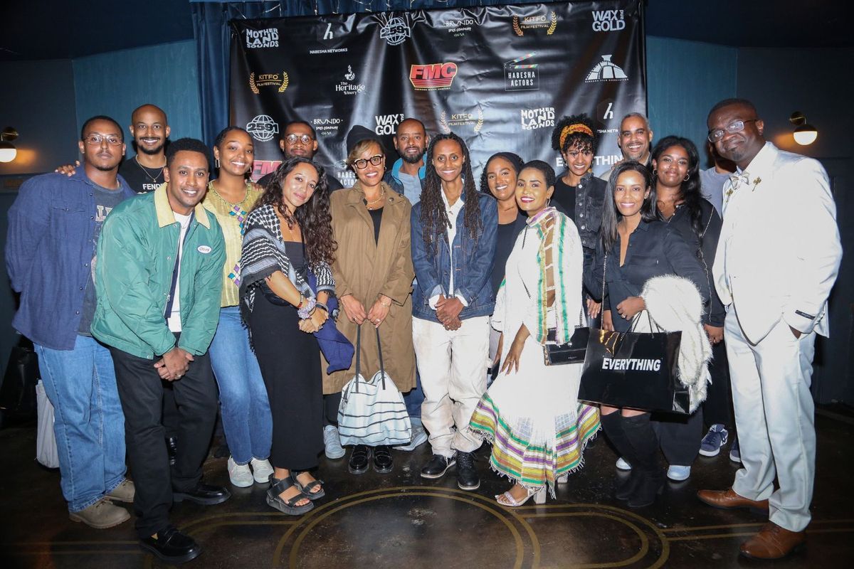 A group of people stands together smiling in front of a KITFO Film Festival backdrop at an event hosted by Kitfo TV.