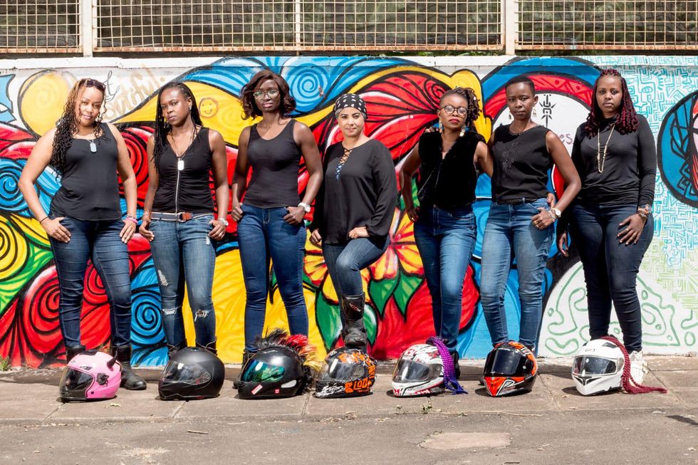 A group of women motorcyclists pose with their helmets in front of their feet. 
