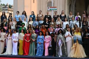 A large group of Miss World 2025 contestants pose on a grand staircase, dressed in a wide variety of traditional and formal attire that reflects their diverse cultures and styles. The background shows the ornate facade of an Indian building. The women wear name badges and smile or pose confidently for the camera.