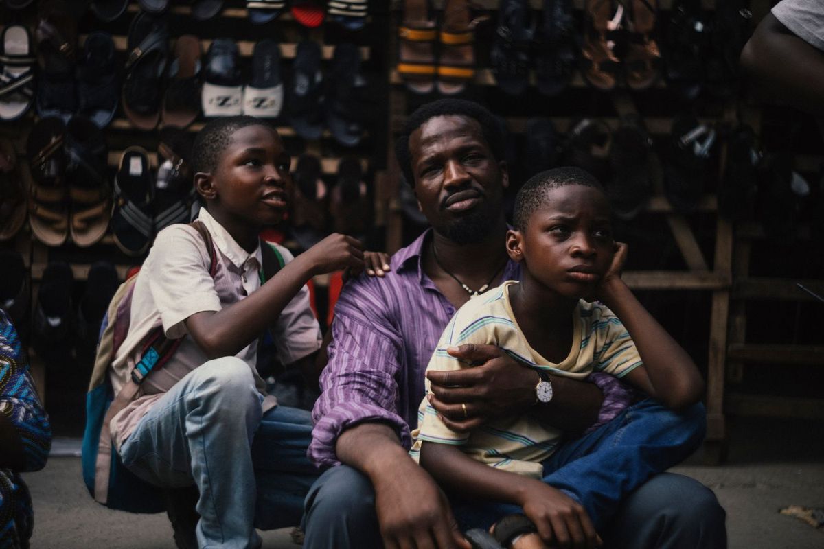 A man sits in front of a shop with two young boys