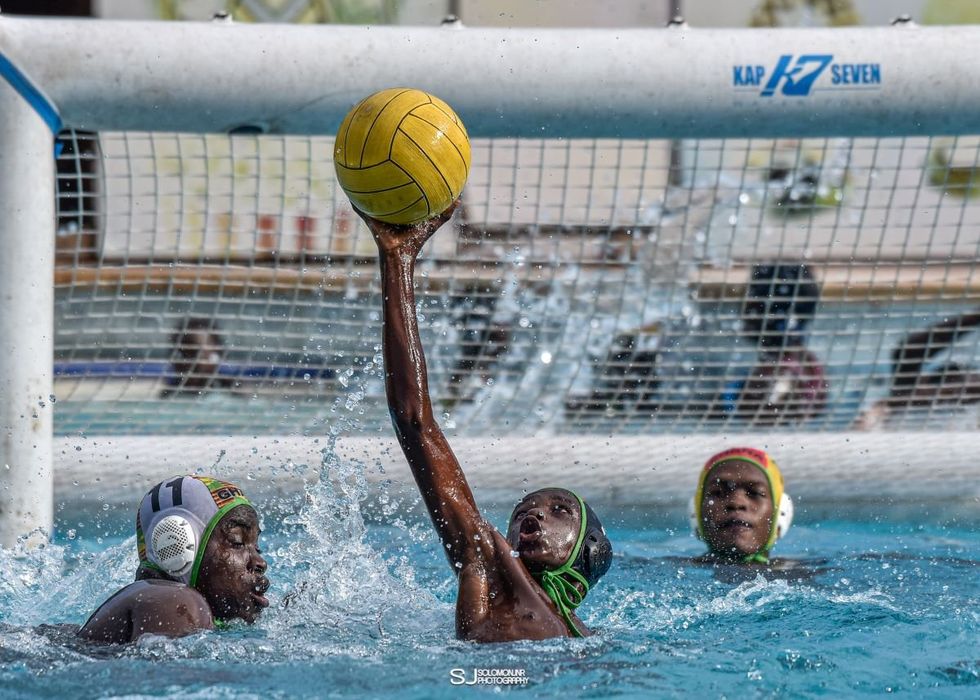 A photo of a teenage water polo player stretching to catch the ball.