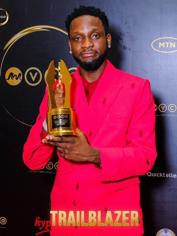 A photo of Chimezie Imo holding his Trailblazer Award plaque at the 2024 Africa Magic Viewers' Choice Awards (AMVCA). 