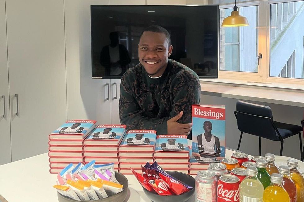 A photo of Chukwuebuka Ibeh resting on a table surrounded by multiple copies of his books, snacks, and drinks.