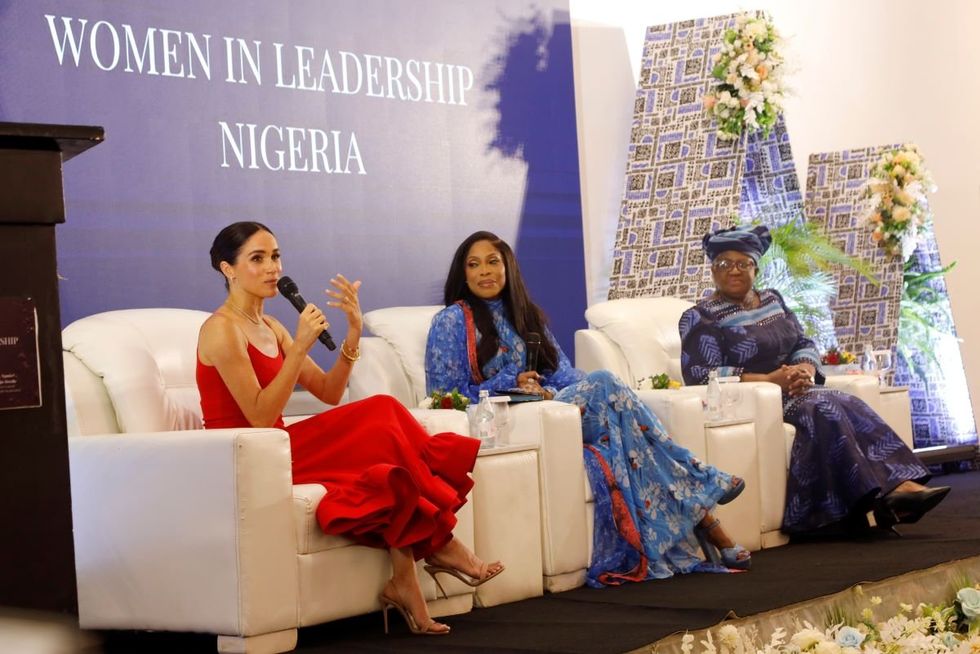 A photo of Meghan Markle speaking on stage with Dr Ngozi Okonjo Iweala and Mo Abudu beside her.