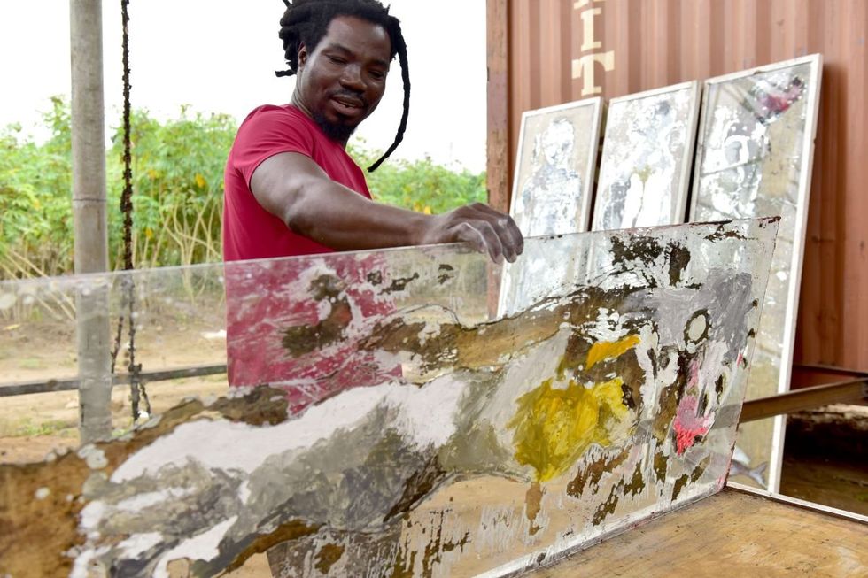 A photo of Sadikou Oukpedjo with his hands on one of his paintings done on old mirrors.