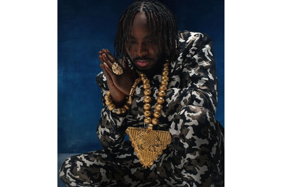 A picture of Fuse ODG captured in a near-kneeling position while wearing a large gold chain and gold bracelets and ring.