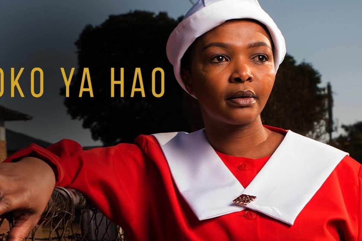 A portrait of Simphiwe Dana leaning on a gate and wearing red church uniform. 