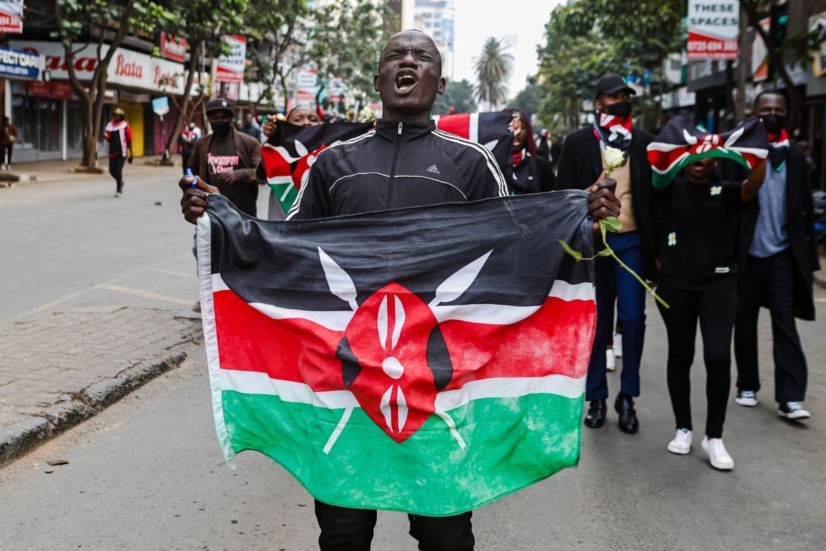 A protester displays a Kenyan flag during a protest, with other protesters in the background
