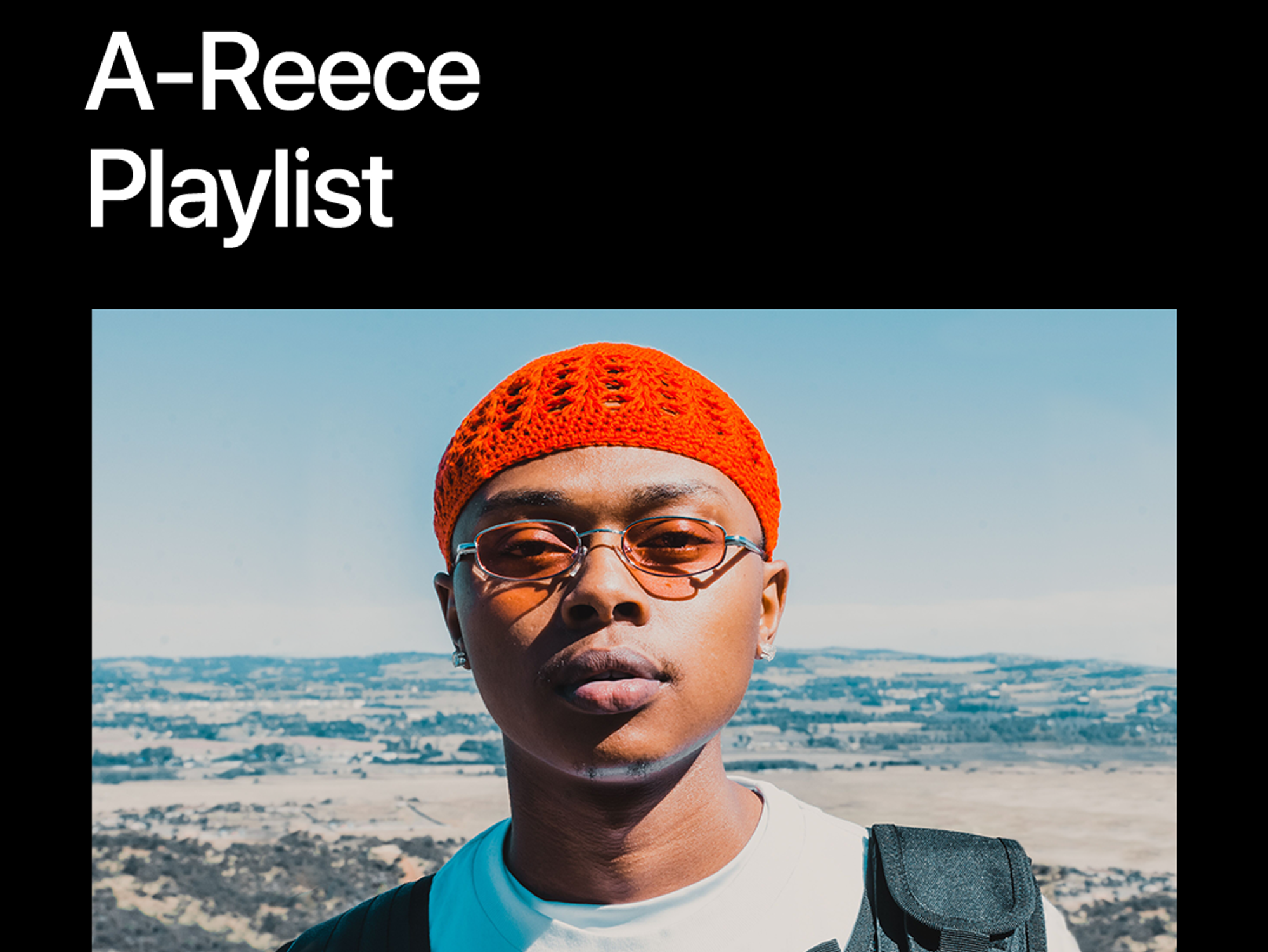 A-Reece sunkissed, wearing an orange woolen hat, glasses and a white t-shirt. 