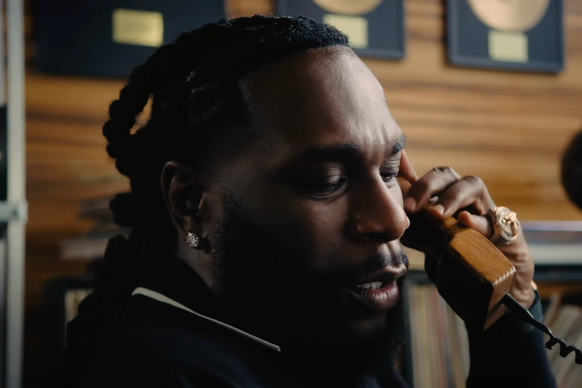 A screenshot of Nigerian artist Burna Boy in the ad video for a new collection by Swiss sportswear brand On, showing the music star holding a telephone in an office.