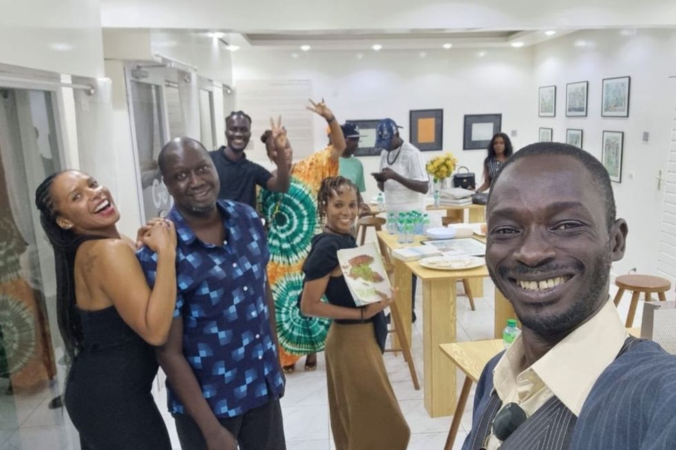 A selfie photo with people smiling brightly behind a white background filled with artwork.
