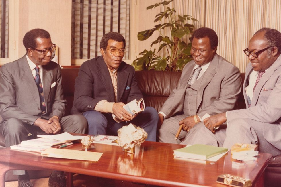 A sepia-toned image of John Blay-Miezah sitting on a couch surrounded by investors and associates.