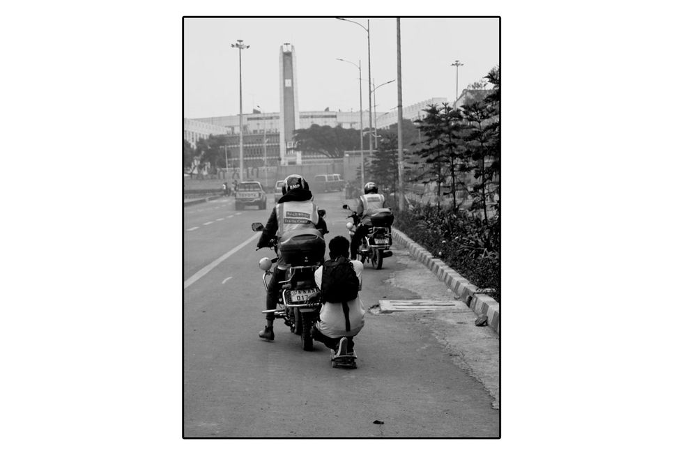 A skateboarder holds on to the back of a motorized scooter going down the road. 