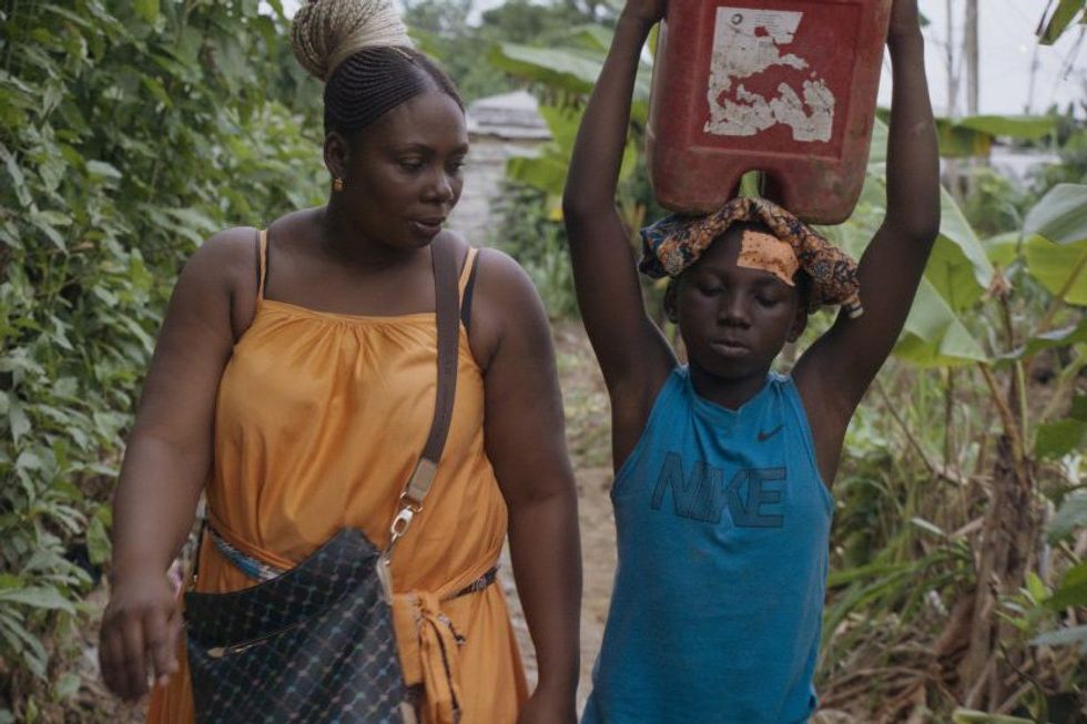 A still from the film, 'Mambar Pierrette,' of a woman walking next to a girl carrying a bucket on her head.