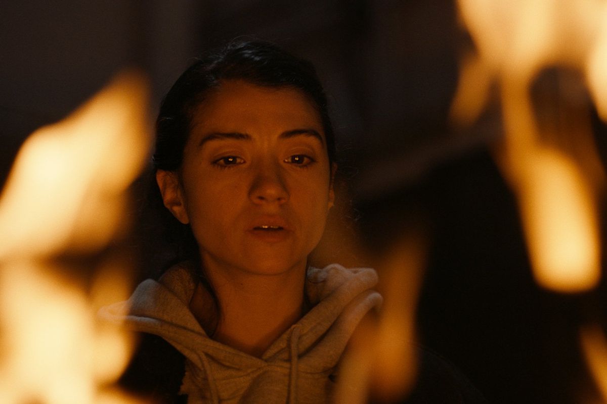 A still from the film of a woman looking into flames.