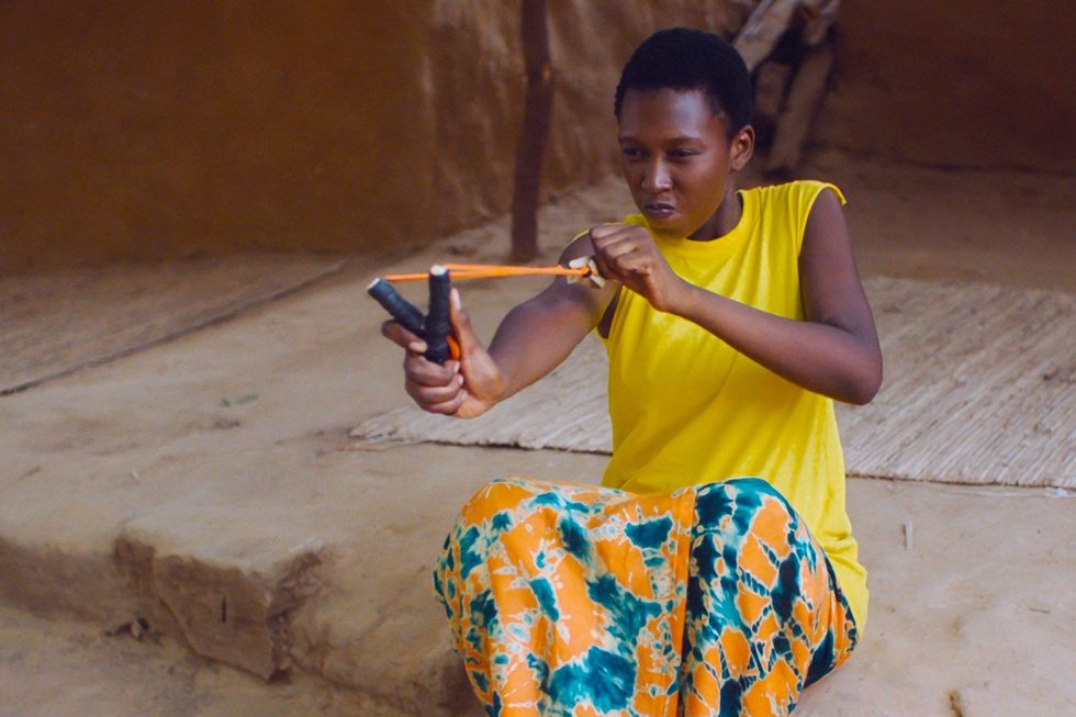 A still from the film of a woman pulling back a slingshot.