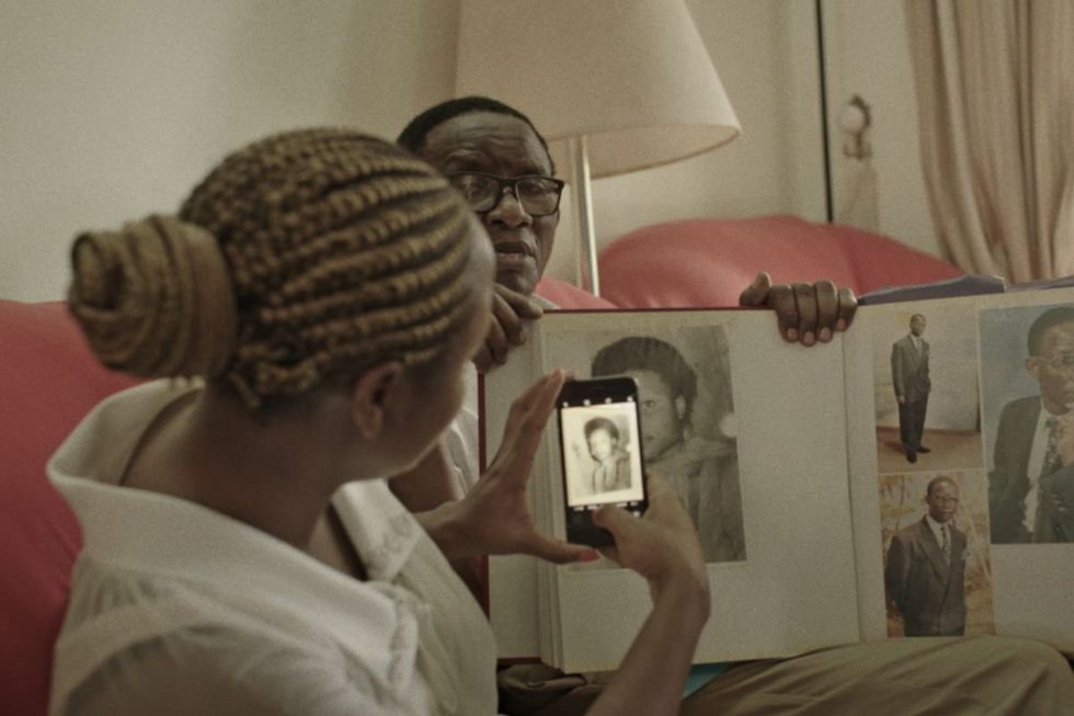 A still from \u2018Death of a Saint\u2019 showing Patricia Bbaale Bandak taking a picture of her mum in an old photo album held up by a man.