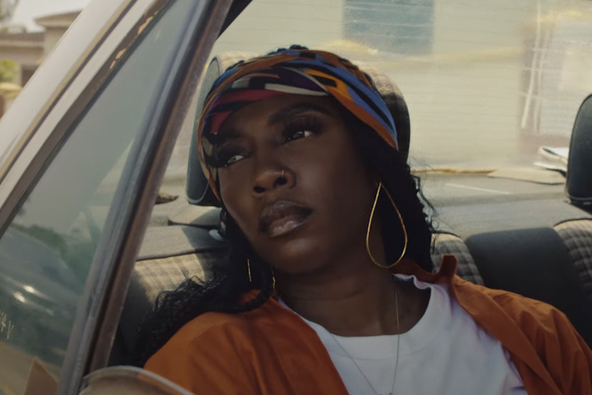  A still from “Water and Garri” trailer, showing Tiwa Savage in the backseat of a car, looking out the window.