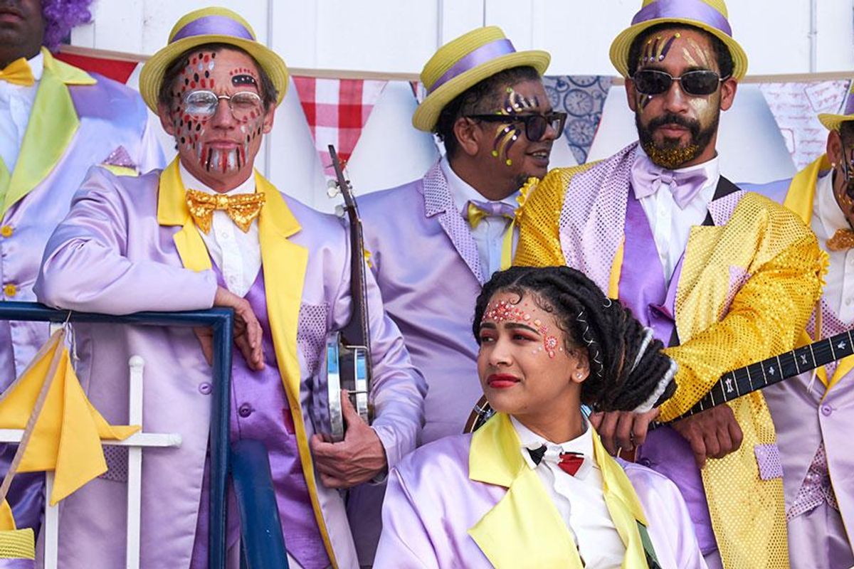 A still image from the film The Umbrella Men of minstrels in colorful outfits, waiting to play their instruments