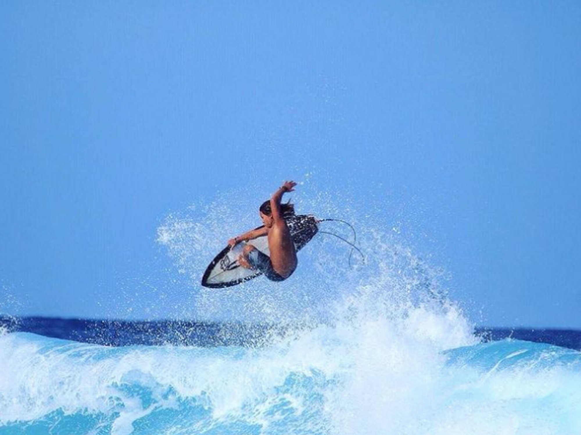 A surfer rides a wave with his hand in the air.