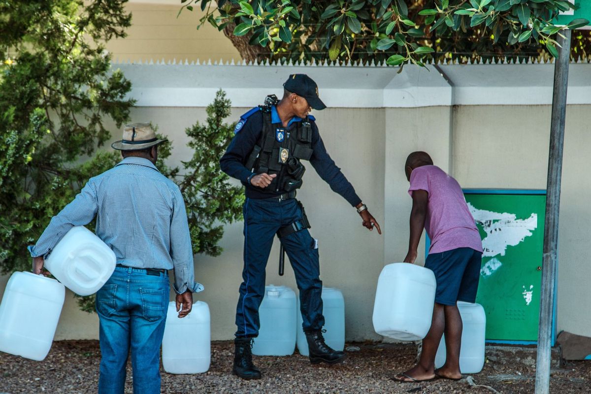 A uniformed man points to citizens carrying large empty jugs for water.  