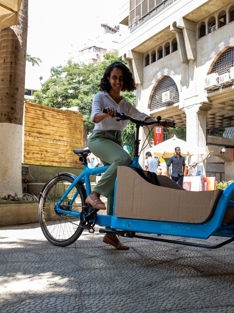 A woman sits on the seat of a long bike in an open marketplace. 