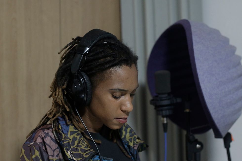 A woman with dreadlocks in front of a mic with headphones on during a recording session. 