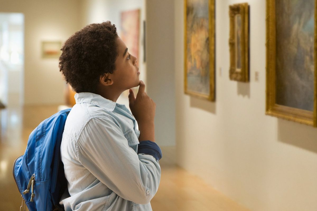 A young Black boy looks thoughtfully at a painting in a museum gallery. Stock photo. 