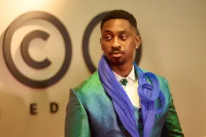 A young man in a green suit with purple embellishment looking off camera.