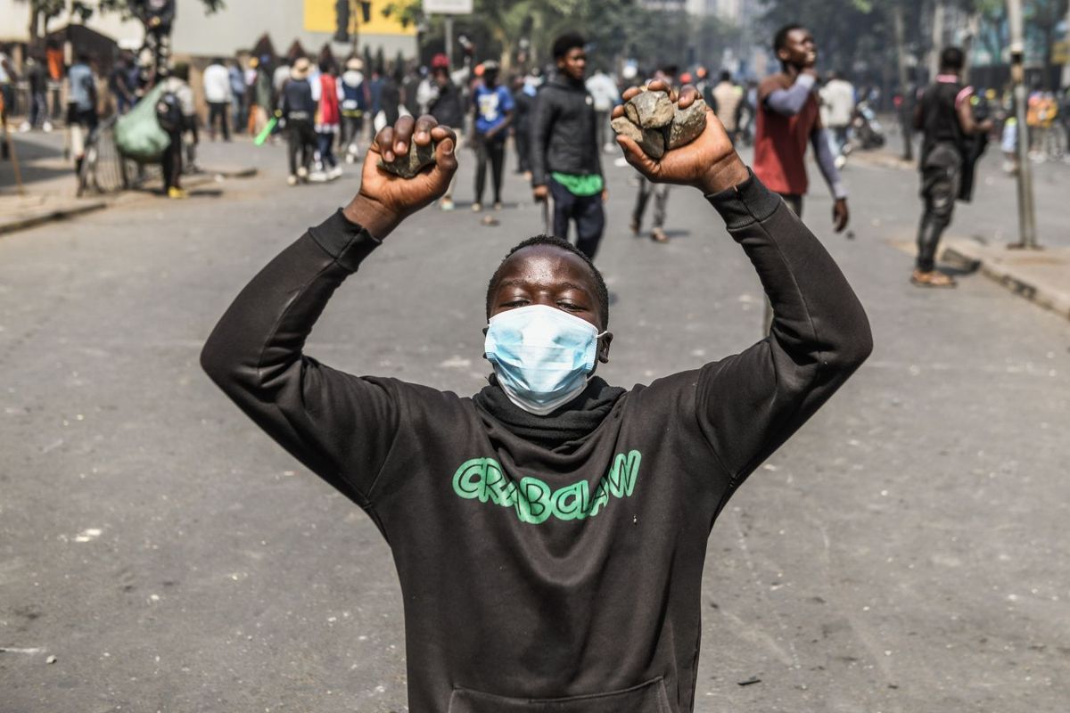 A young man with a mask partially covering his face kneels with his hands up, holding rocks, during protests against police brutality at the Central Business District in Nairobi, Kenya.