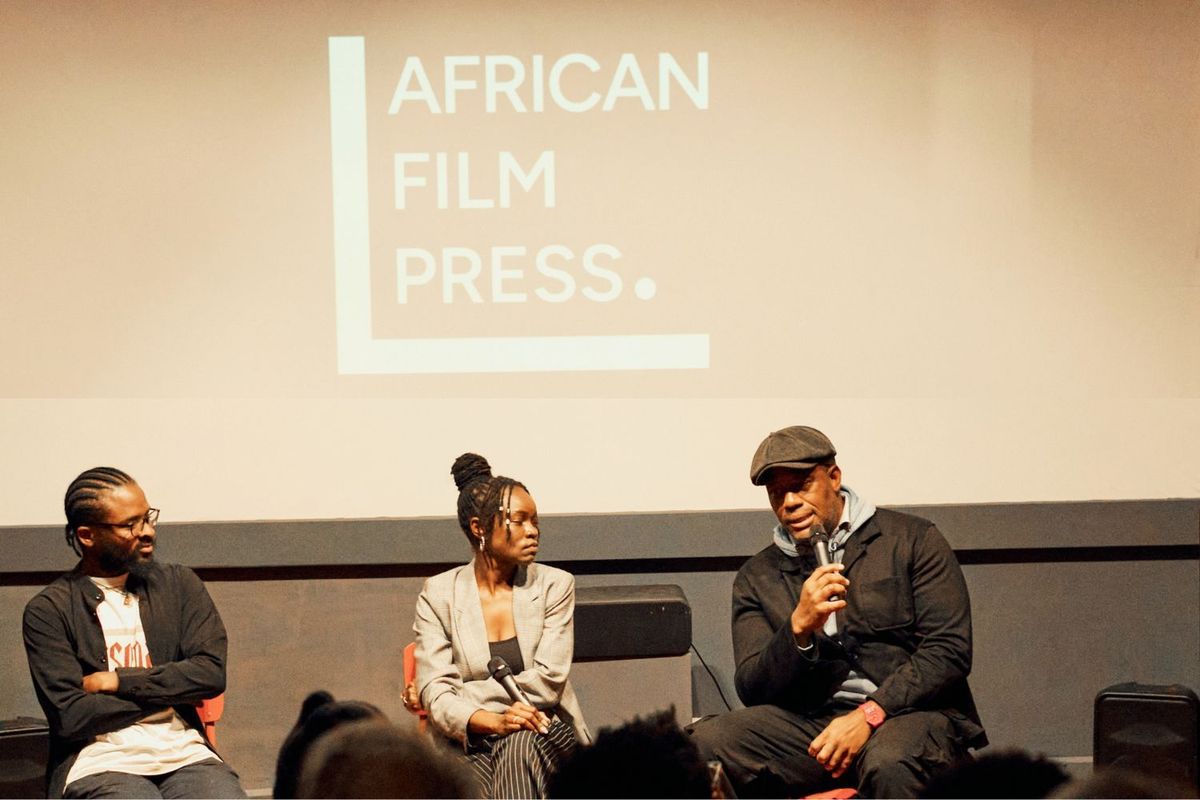 African Film Press (AFP) co-founders Ikeade Oriade (left), Jennifer Ochieng (middle), and Tambay Obenson (right) converse during a panel discussion at an AFP invite-only event in Nairobi, Kenya, on August 22, 2025. They’re seated in front of a projector showing the African Film Press logo on it.
