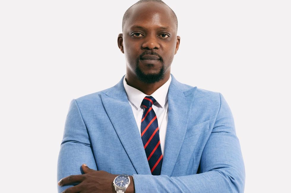 Akinyemi Ayinoluwa poses for the camera while wearing a sky blue suit behind a white studio background.