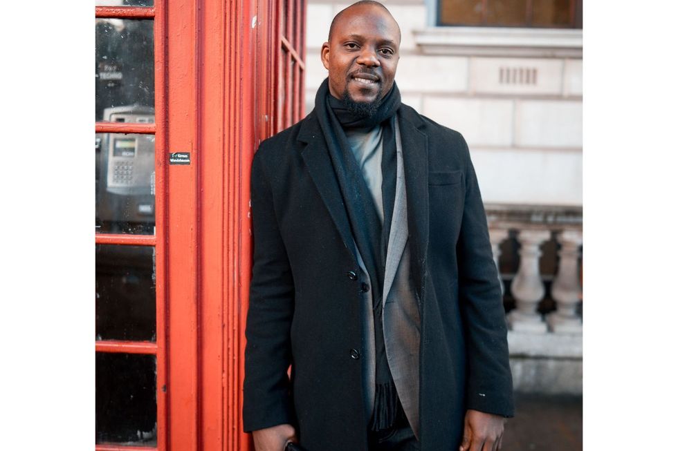 Akinyemi Ayinoluwa poses next to a red phone booth.