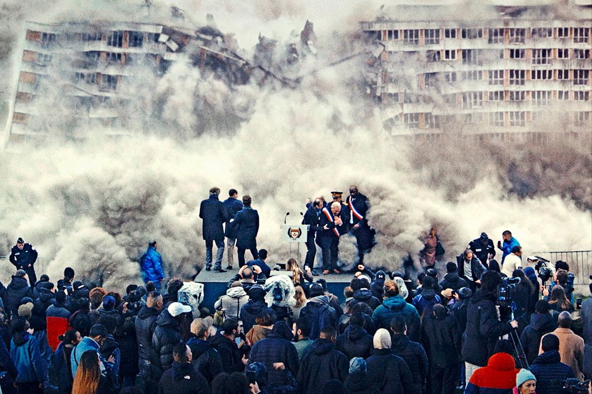 An image from the film of a building being demolished in front of a group of people. 