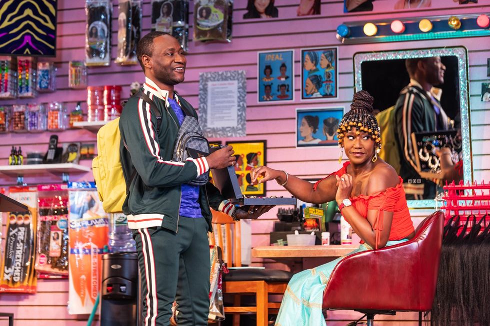 An image from the play of a man and a woman in a hair braiding shop; the woman is looking off to the side.