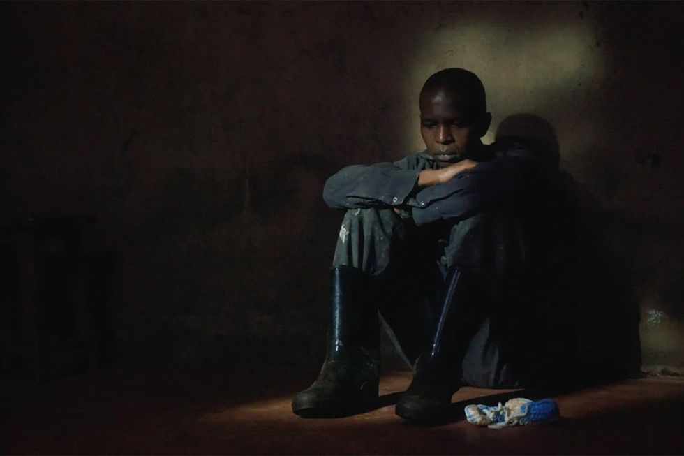 An image of a man sitting in the dark, wearing gumboots, looking forlorn.