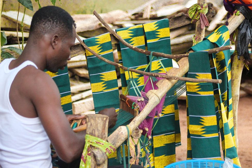 An image of a man weaving green and gold kente .