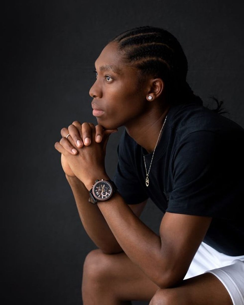 An image of Caster Semenya, dressed in a black shirt and white shorts, sitting down with her hands on her chin, looking pensive.