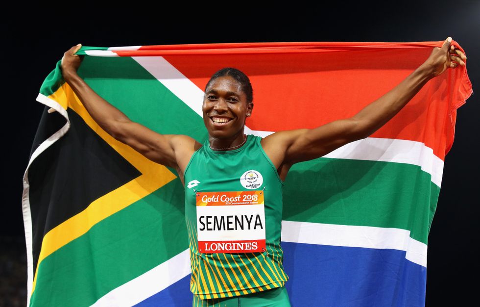 An image of Caster Semenya holding the South African flag up behind her back, smiling.