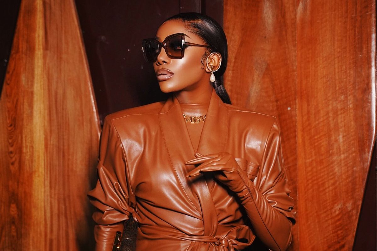 An image of Chioma Ikokwu in a brown leather outfit with her head turned to the side, wearing sunglasses.