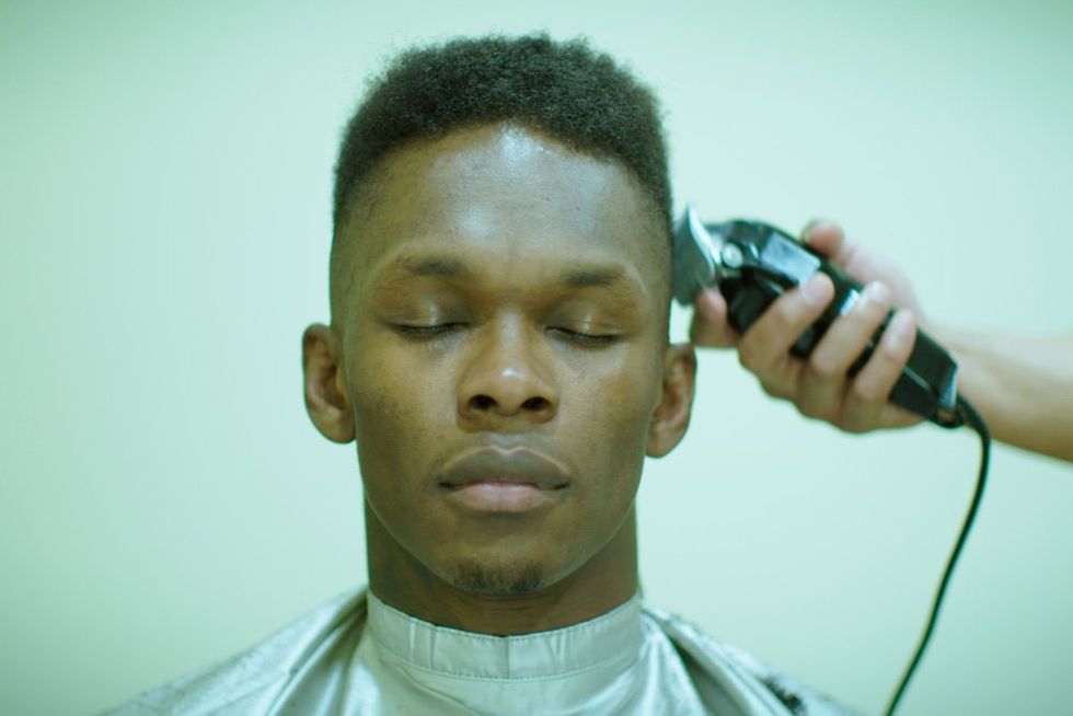 An image of Israel Adesanya with his hair being shaved.